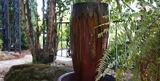 A large wooden vase is sitting in a garden surrounded by trees.