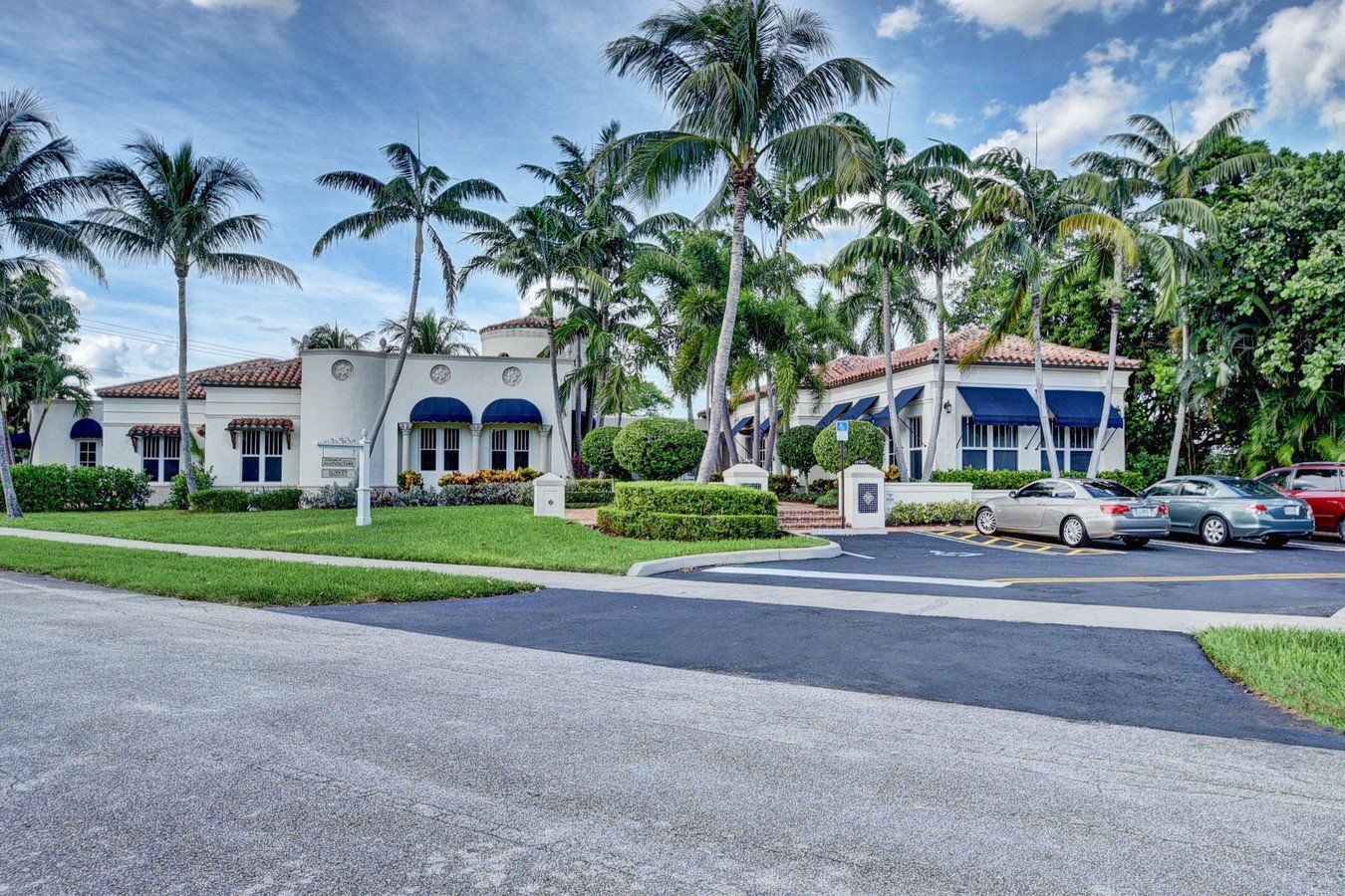 A white building with blue awnings is surrounded by palm trees