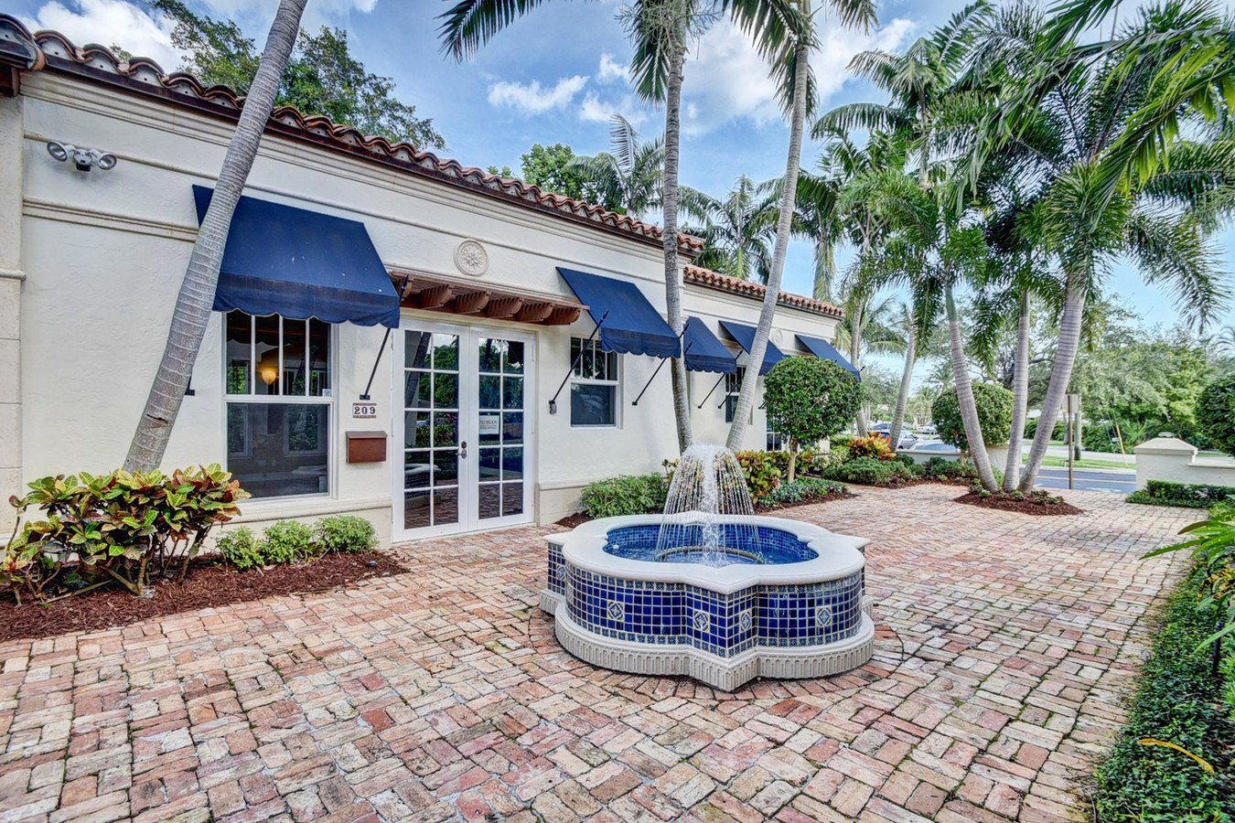 A white building with blue awnings and a fountain in front of it.