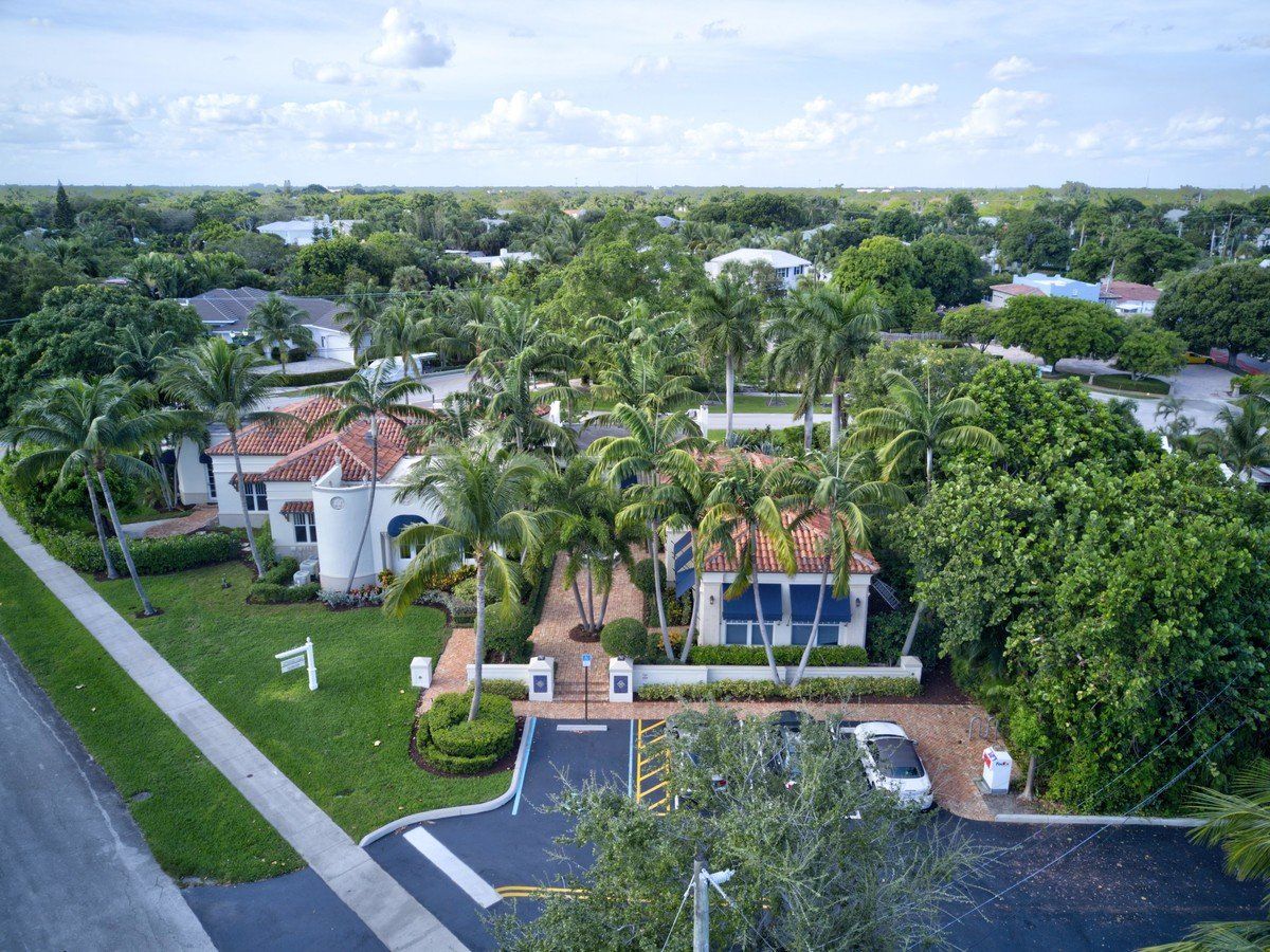 An aerial view of a house in a residential area surrounded by palm trees.