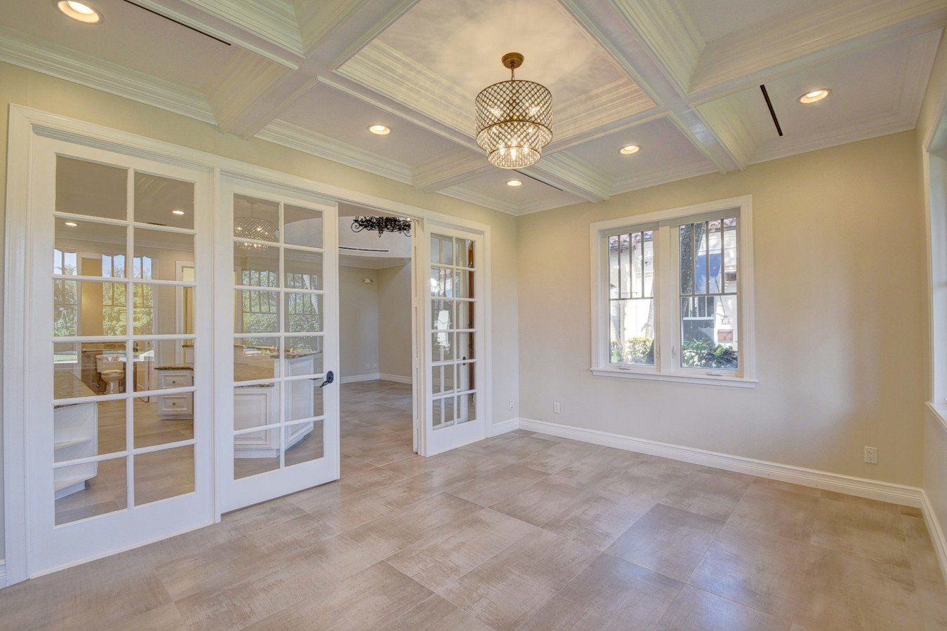 An empty room with french doors and a chandelier hanging from the ceiling.