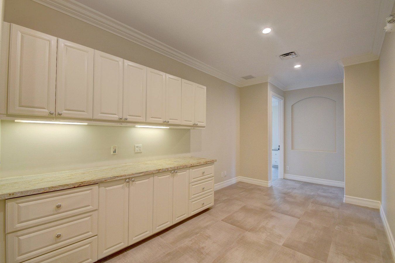 An empty kitchen with white cabinets and a tile floor.