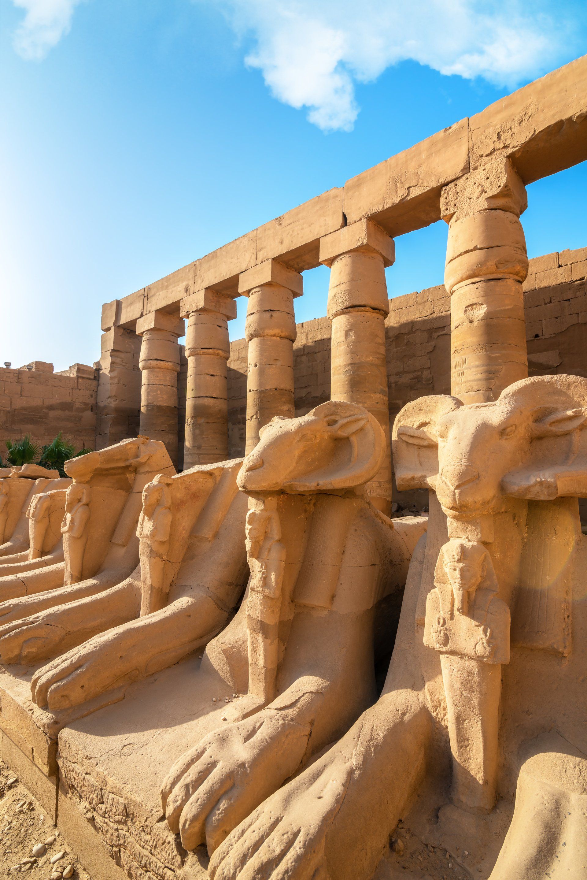 Ancient Egyptian stone statues and columns under a bright blue sky