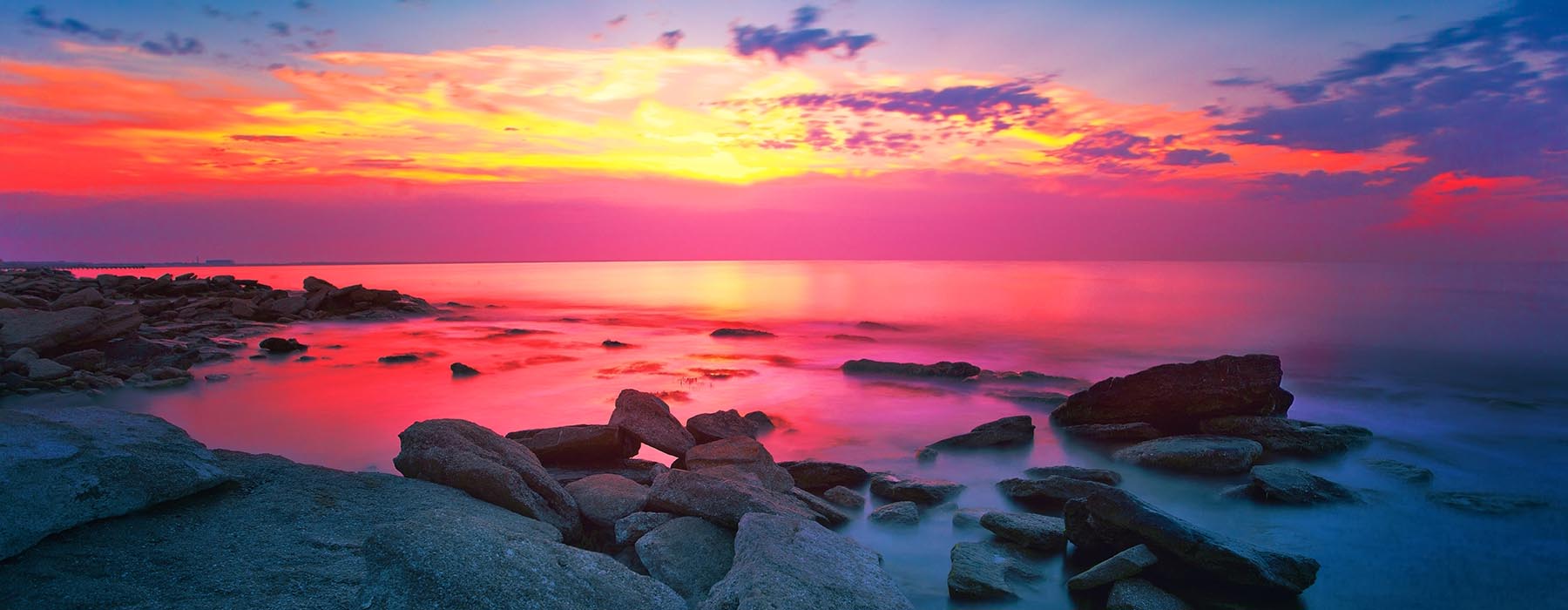 A colorful sunset over the ocean with rocks in the foreground.