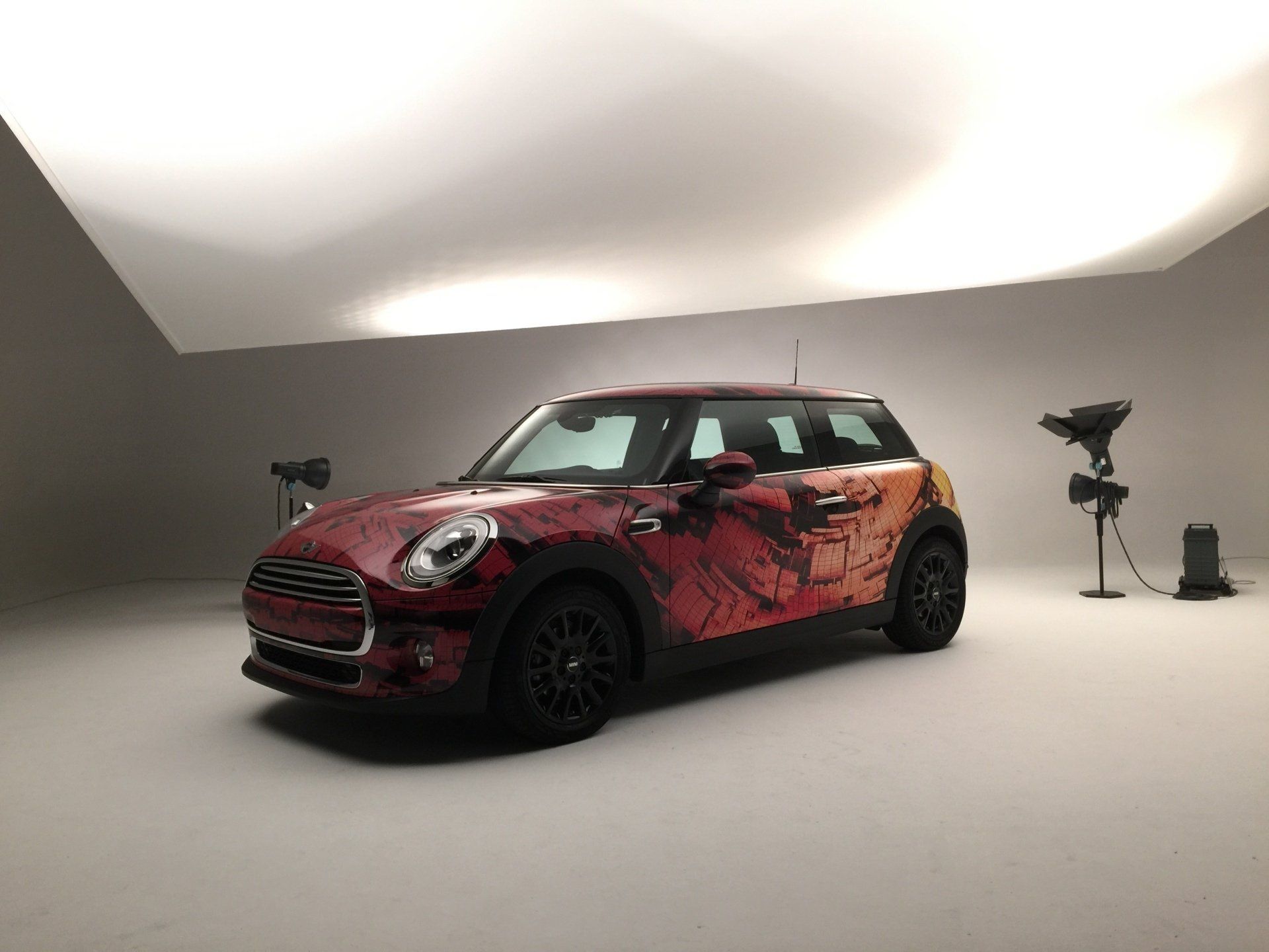 Red and orange wrapped patterned Mini Cooper car in a studio setting with lighting equipment.