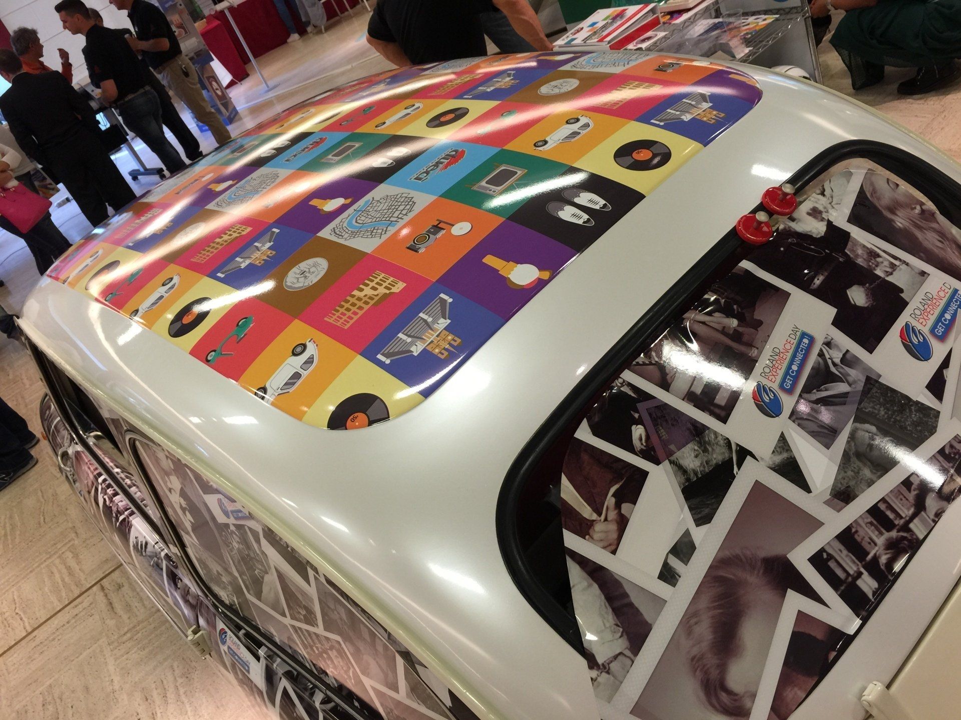 Car roof covered in colorful squares with album covers, parked indoors.