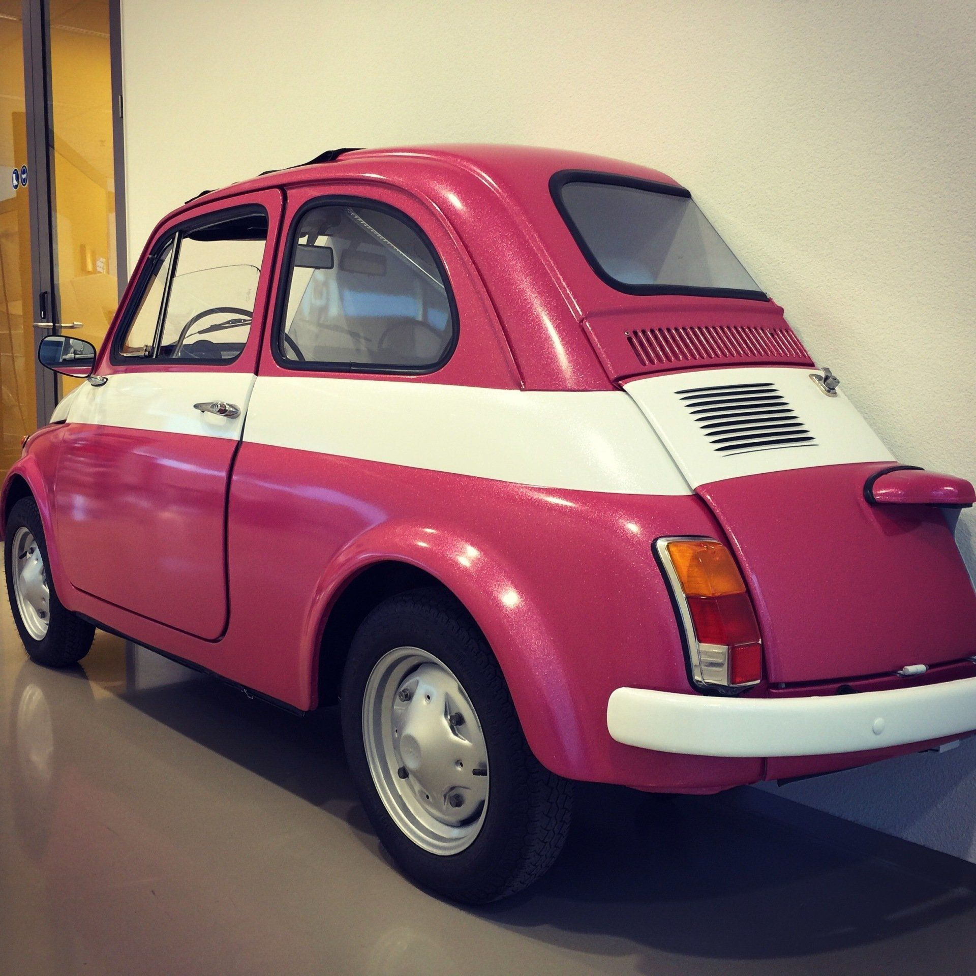 Pink and white wrapped vintage Fiat 500, parked indoors.