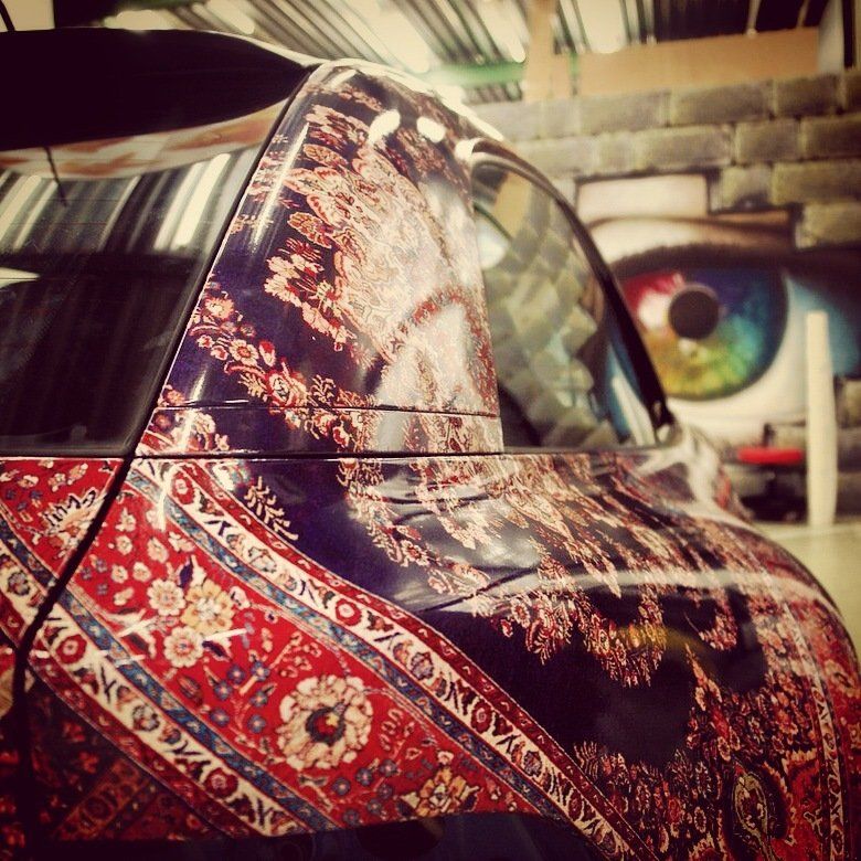 Car with oriental rug design wrap, parked inside, mural of a colorful eye in the background. BMW Z3 M. Wrap Maniacs