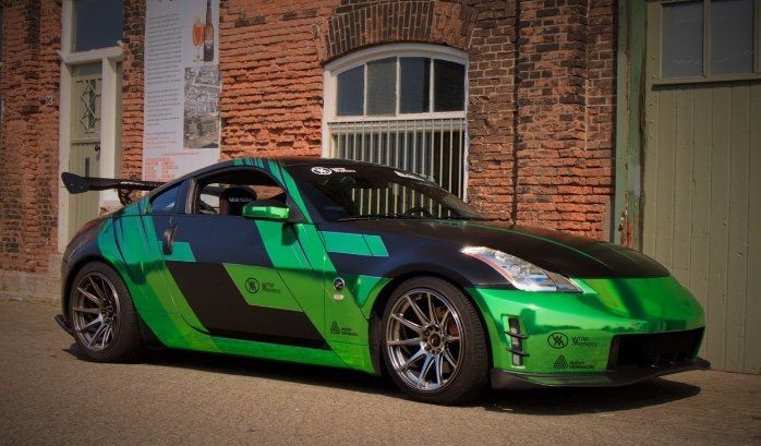 Chrome green and black wrapped Nissan 350Z sports car with a spoiler parked in front of a brick building. Wrap Maniacs.