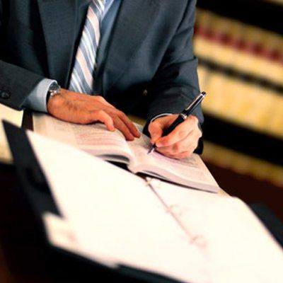 A person in a suit writing in a book at a desk, law books in the background.