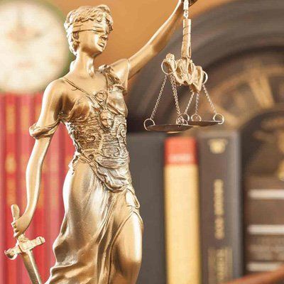 Statue of Lady Justice, gold, blindfolded, holding scales and sword, in front of books.
