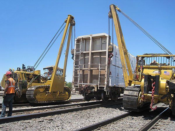 Hulcher sidebooms rerail a rail car at a rail yard following a derailment