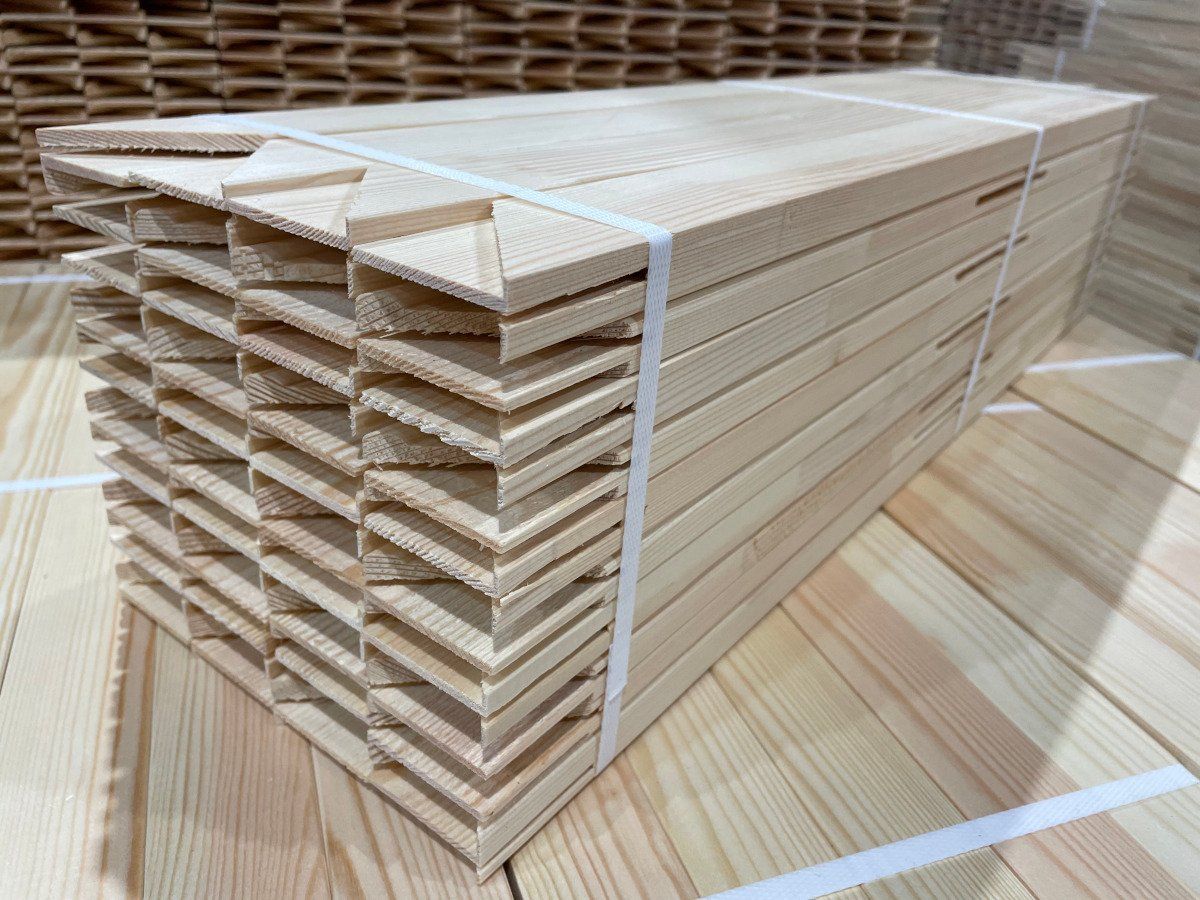 Stacked wooden slats or panels bundled with white straps in a warehouse setting.
