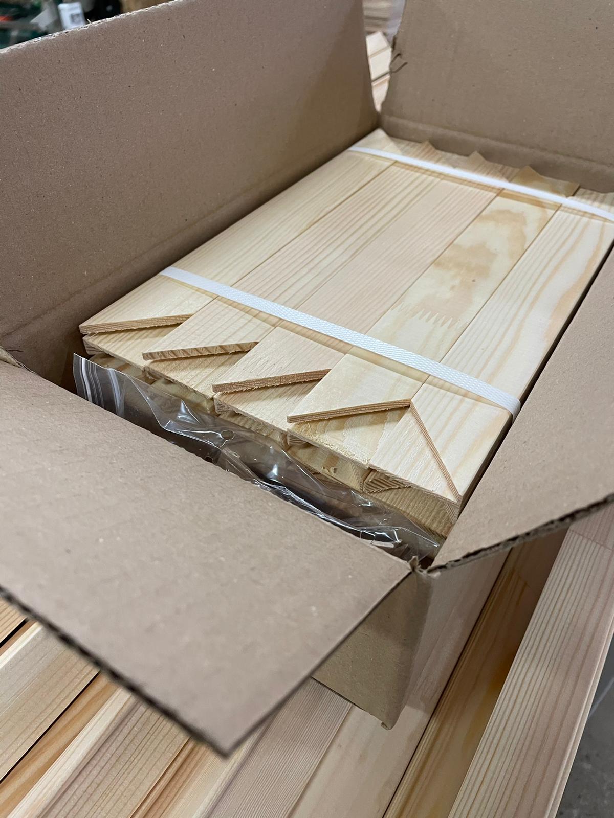 Open cardboard box with stacked light wooden slats wrapped in plastic and secured with tape