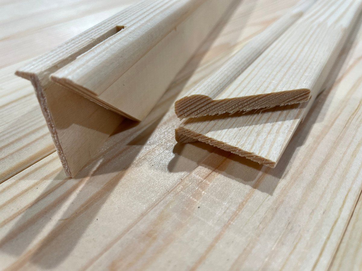 Wooden trim molding pieces stacked on a light pine surface, showing angled edges.