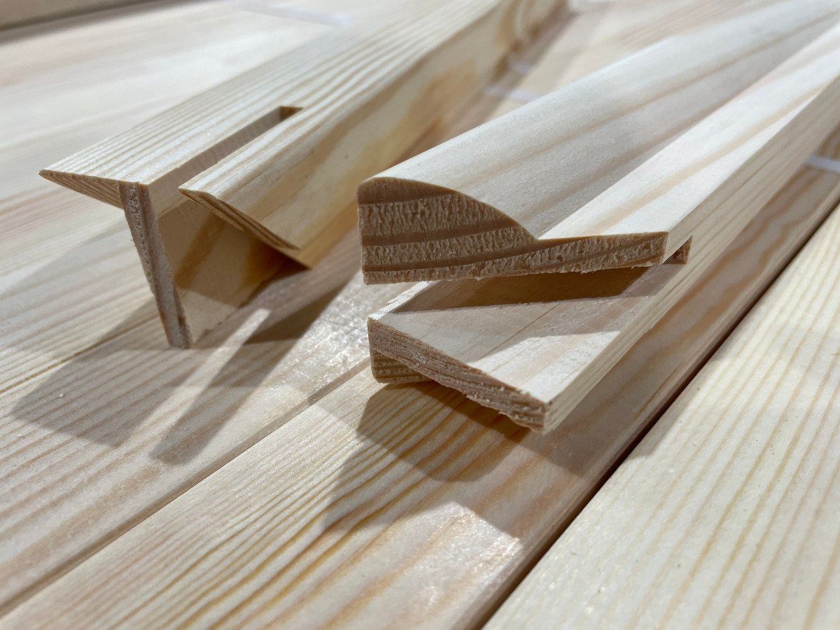 Wooden trim moldings on a light wood surface, shown in close-up.