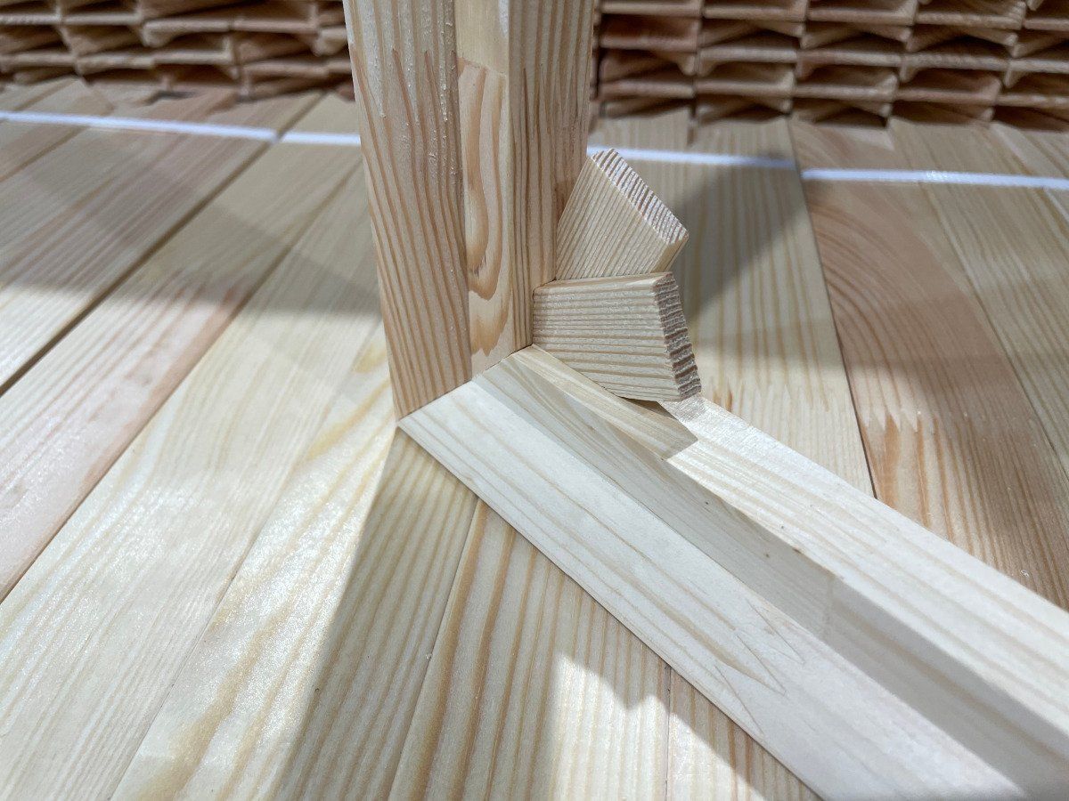 Wooden furniture joint with angled braces on a light wood floor, close-up.