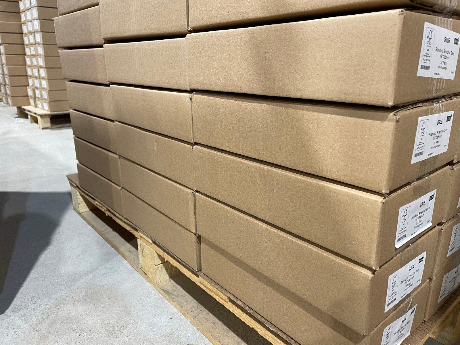 Stacked brown cardboard boxes on a wooden pallet in a warehouse aisle.