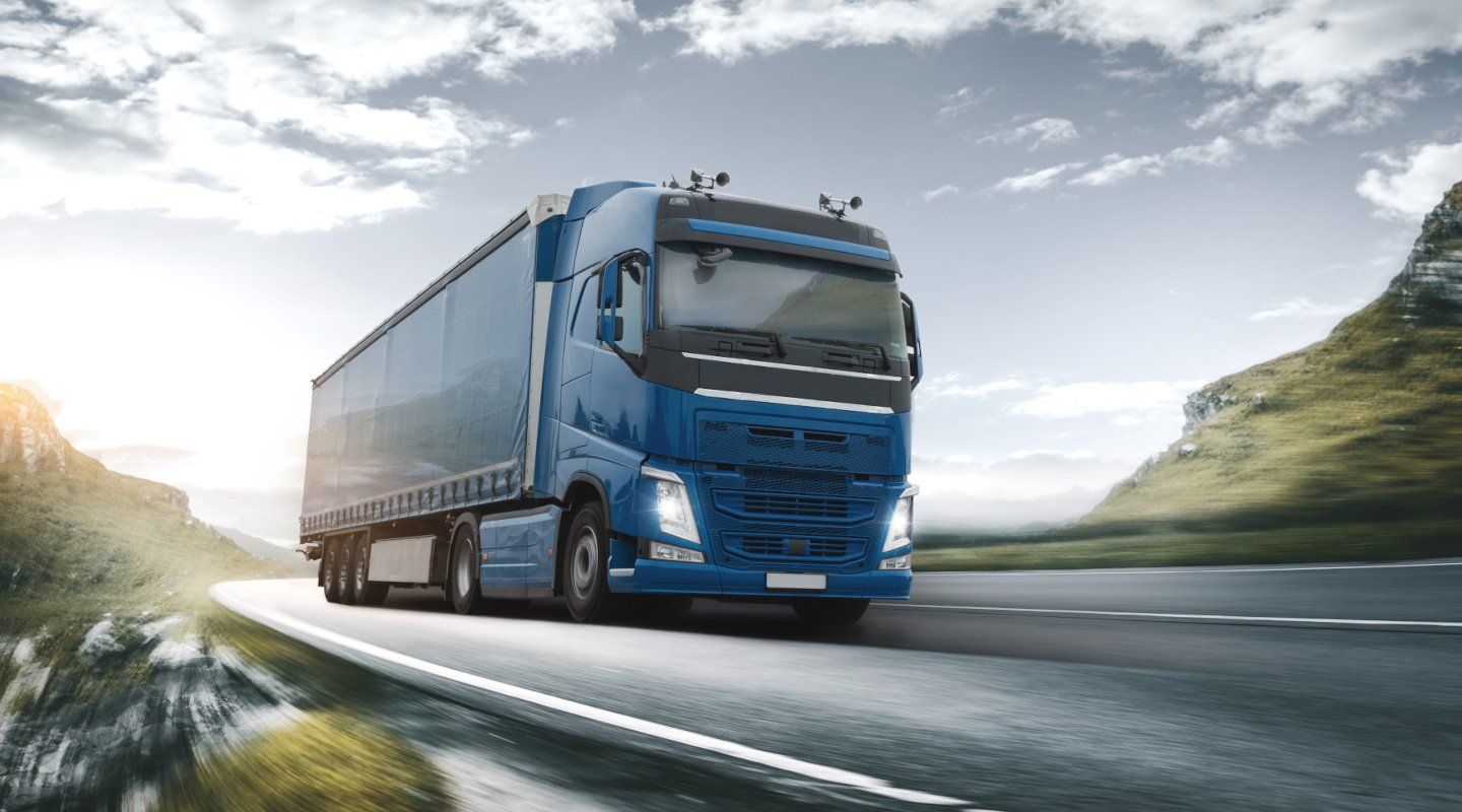 Blue semi-truck driving on a mountain highway under a cloudy sky