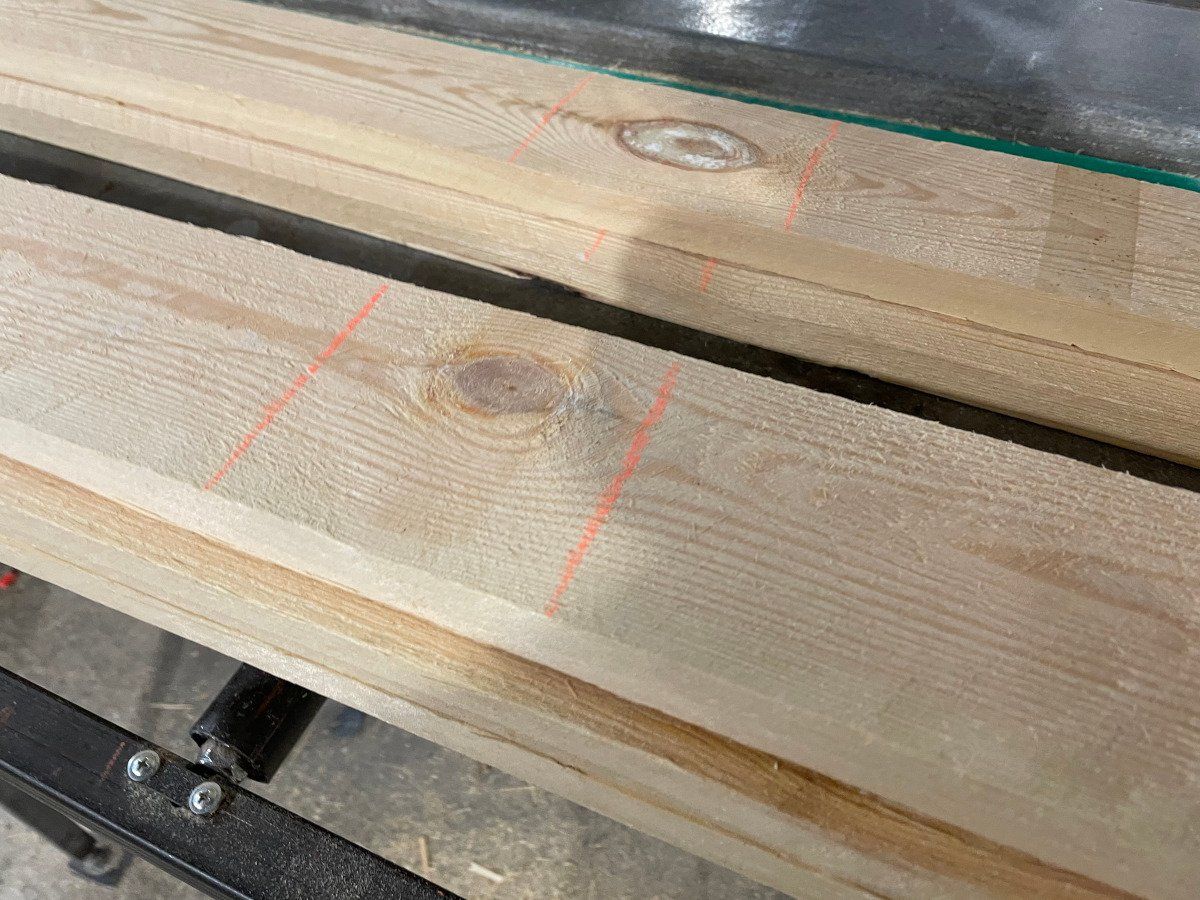 Stacked light wooden planks with knots and red chalk marks on a workbench