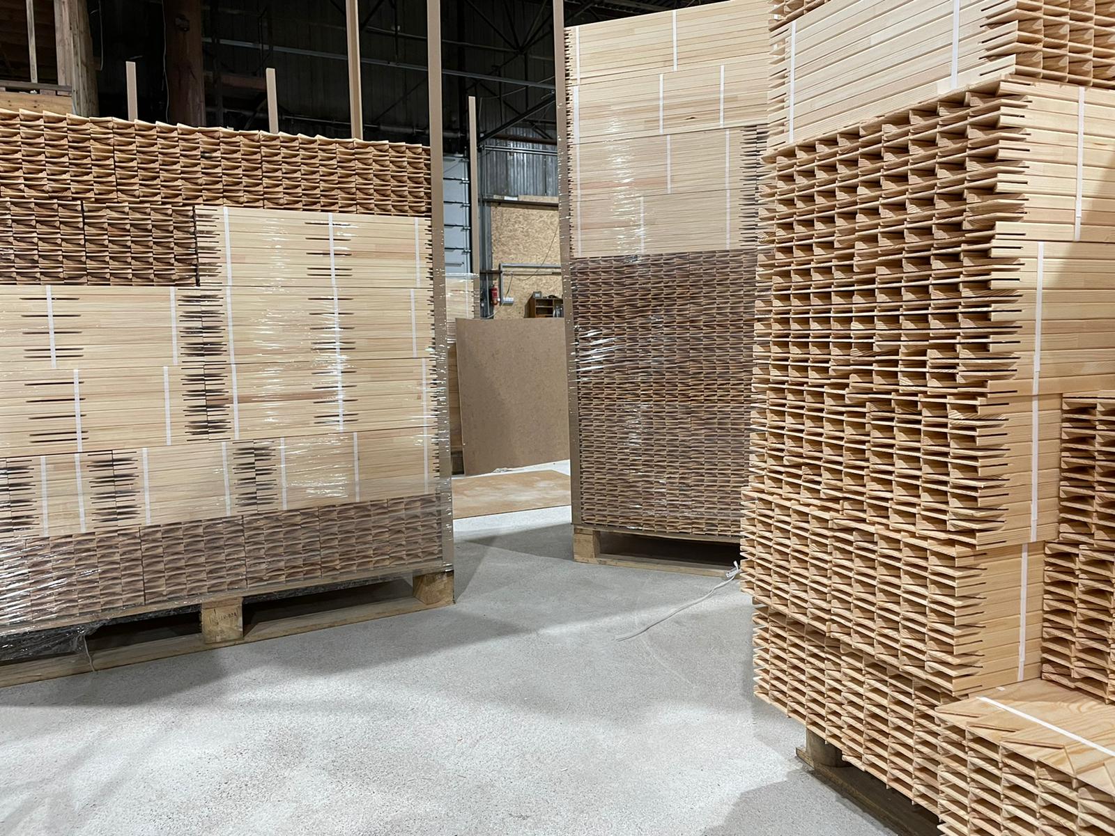 Stacks of wooden crates and pallets in a warehouse aisle, with a concrete floor and shelving in the background