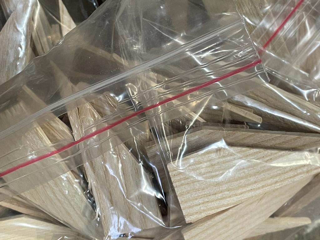 Plastic-wrapped stack of light wood boards or planks with a red strap across the top.