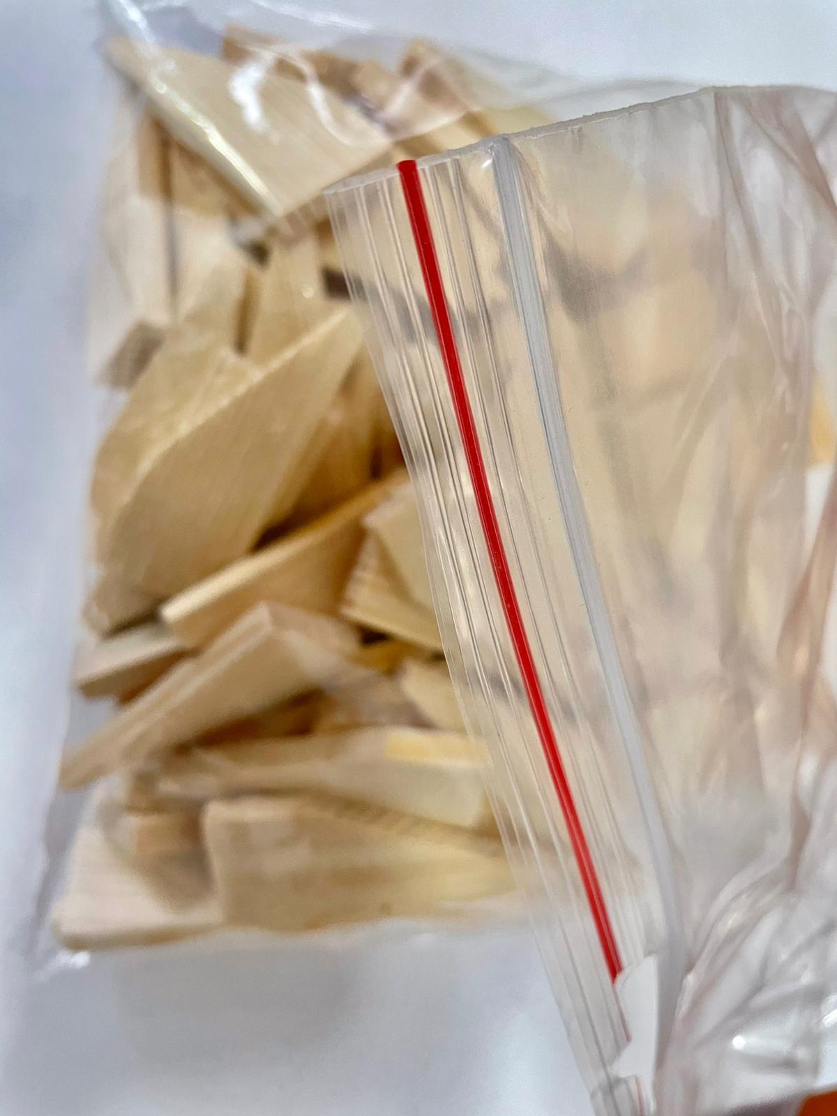 Clear plastic bag holding small beige wooden wedges on a white surface