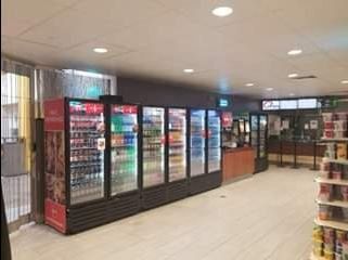 A convenience store interior with beverage coolers, a counter, and shelves of items. Bright overhead lighting.