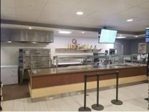 Cafeteria food service area with long serving counter, stainless steel appliances, and mounted TV.