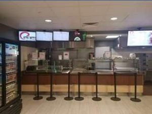 A cafeteria food counter with monitors above. A cooler is on the left.