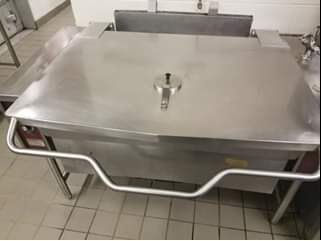 Large stainless steel commercial tilt skillet in a kitchen, with a closed lid and safety bars.
