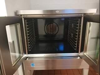 Stainless steel commercial oven with open glass doors, revealing interior racks and fan.