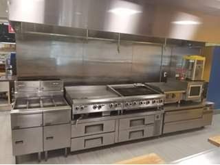 Stainless steel commercial kitchen cooking equipment, including stovetops, griddle, and warming ovens.