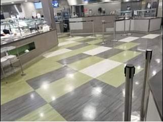 Checkerboard-tiled floor in a commercial kitchen/cafeteria, with service counters and queue stanchions.