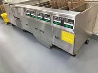 Stainless steel commercial fryer with multiple compartments and digital controls, on a gray floor.
