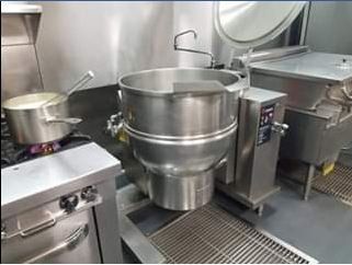 Commercial kitchen with large stainless steel tilting kettle and stovetop.
