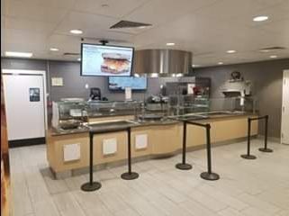 Cafeteria food serving area with stainless steel hood, monitors, and stanchions.