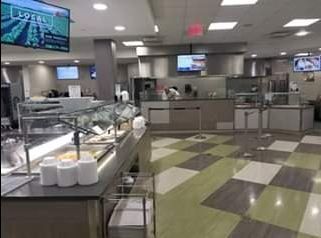 Cafeteria with food service lines, stainless steel counters, checkered floor, and TVs.