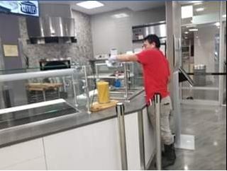 A person in a red shirt reaches towards a serving counter in a commercial kitchen setting.