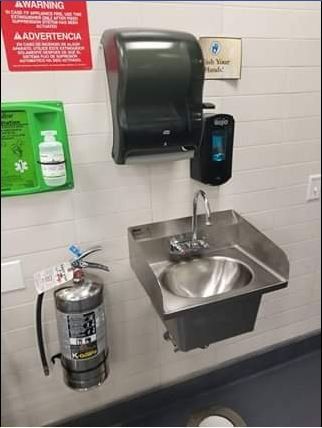 A wall-mounted handwashing station with a sink, soap dispenser, and paper towel dispenser. Fire extinguisher nearby.