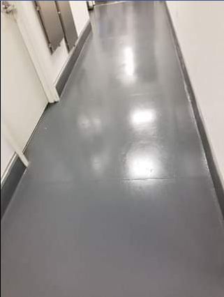 Grey, shiny floor of a hallway with white walls and silver metal fixtures on the left.