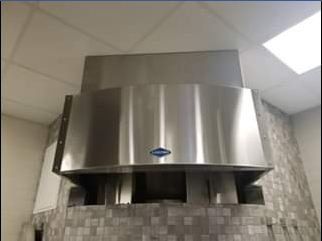 Stainless steel commercial range hood mounted above a gray tile structure.