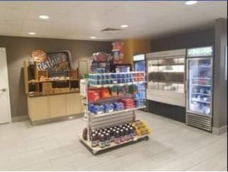 Hotel convenience store with snacks, drinks, and refrigerated goods. Light wood shelves and neutral walls.
