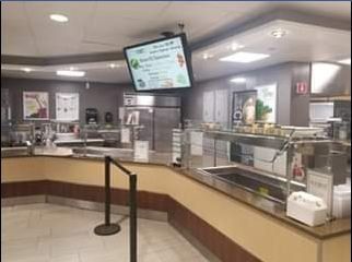 A cafeteria with food service stations. A digital menu hangs from the ceiling.