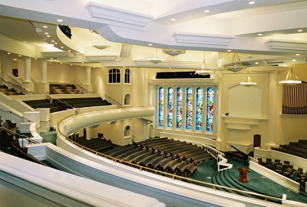 Interior view of a church with a curved balcony, rows of pews, stained glass, and a podium.