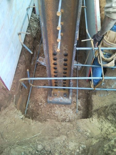 Construction worker near a metal beam, rebar supports in a dirt foundation.