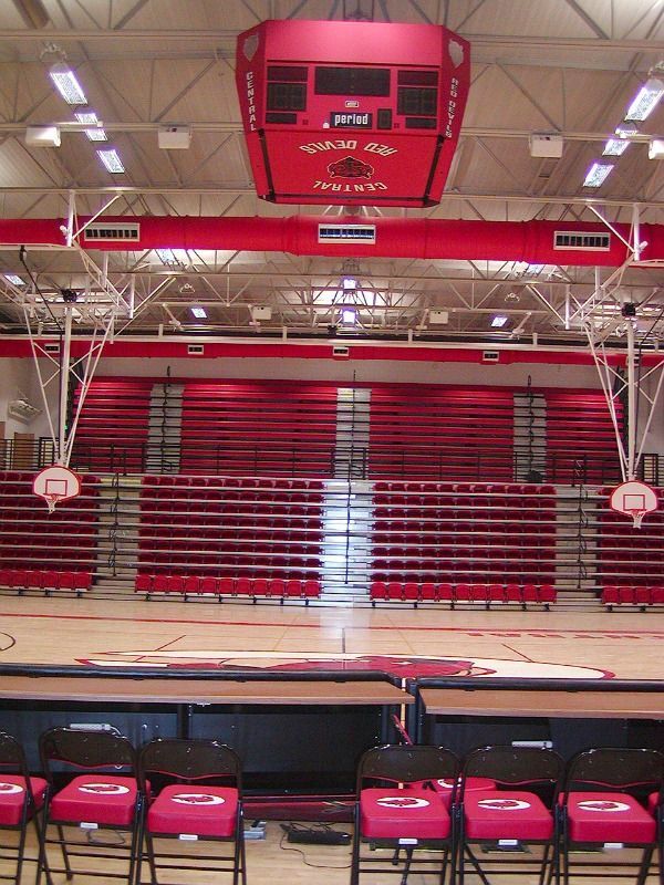 Basketball court with red bleachers, scoreboard, and chairs.