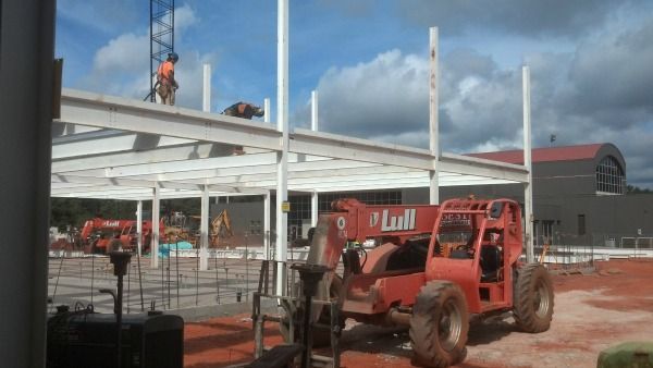 Construction site with workers on beams, a Lull telehandler, and a building under construction.