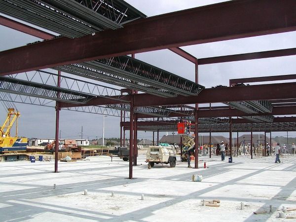 Construction site with steel framework, workers, and machinery under cloudy sky.