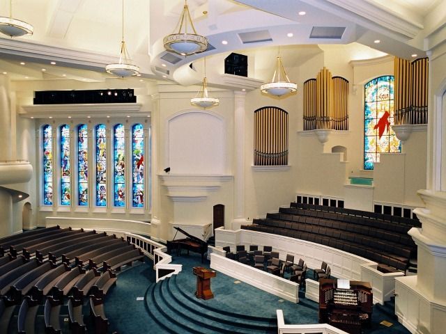 Interior view of a church sanctuary with pews, stained glass windows, and organ pipes.